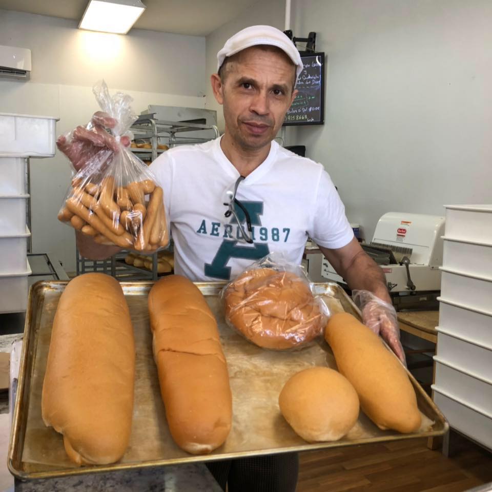 A man is holding packet of bread and there are big loaf of bread on tray too in a bakery